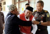 Seorang kakek 71 tahun yang menjadi terdakwa kasus lima burung cendet dari Baluran tampak dipapah oleh petugas kejaksaan dan pendampingnya sebelum memasuki ruang sidang di PN Situbondo, Kamis (11/12/2025), (Assayid Annazili/Liputansatu.id).