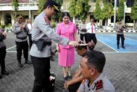 Kapolres Situbondo AKBP Rezi Dharmawan didampingi Ketua Bhayangkari Cabang Situbondo, Ny. Cania Rezi, menyiramkan air kembang kepada personel yang naik pangkat dalam tradisi korps raport di Mapolres Situbondo, Rabu (31/12/2025), (Fia Rahma/Liputansatu.id).