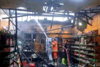 Petugas pemadam kebakaran melakukan proses pemadaman dan pembasahan di dalam toko sembako Afif Mubarok yang terbakar di Jalan Sucipto, Desa Curah Jeru, Kecamatan Panji, Situbondo, Selasa (06/01/2026). Kebakaran tersebut mengakibatkan kerusakan parah pada bangunan toko dan merembet ke rumah warga di sebelahnya, (Fia Rahma/Liputansatu.id).