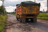 Kondisi jalan rusak parah di jalur Merakurak–Jenu, Tuban, dipenuhi lubang besar dan genangan air saat dilintasi truk bermuatan berat, memicu kekhawatiran keselamatan pengguna jalan, (Aji Swasto/Liputansatu.id).
