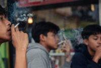 Sejumlah pemuda tampak merokok di sebuah area kafe jalanan dengan suasana santai. Fenomena ini mencerminkan meningkatnya kebiasaan merokok di kalangan anak muda yang dipengaruhi lingkungan pergaulan, (Ilustrasi/Liputansatu.id).
