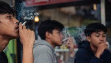 Sejumlah pemuda tampak merokok di sebuah area kafe jalanan dengan suasana santai. Fenomena ini mencerminkan meningkatnya kebiasaan merokok di kalangan anak muda yang dipengaruhi lingkungan pergaulan, (Ilustrasi/Liputansatu.id).